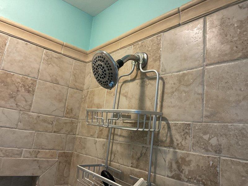 Responded to service call for leaky shower head that had been dripping when shut off for approximately 15 days in a specific bathroom shower. Upon inspection of the chrome shower head mounted in the beige marble-style tiled shower area, diagnosed the issue as a worn internal washer causing water to drip continuously after valve closure. Disassembled the shower head fixture, replaced the deteriorated rubber washer and inspected the shower arm connection for any additional wear or damage. Cleaned mineral deposits from the shower head spray nozzles and internal components to ensure proper water flow and sealing. Reassembled the fixture with proper thread sealant, tested the shower valve operation through multiple on/off cycles, and confirmed no residual dripping occurred. Verified water pressure and spray pattern were functioning normally with no leaks at connection points.