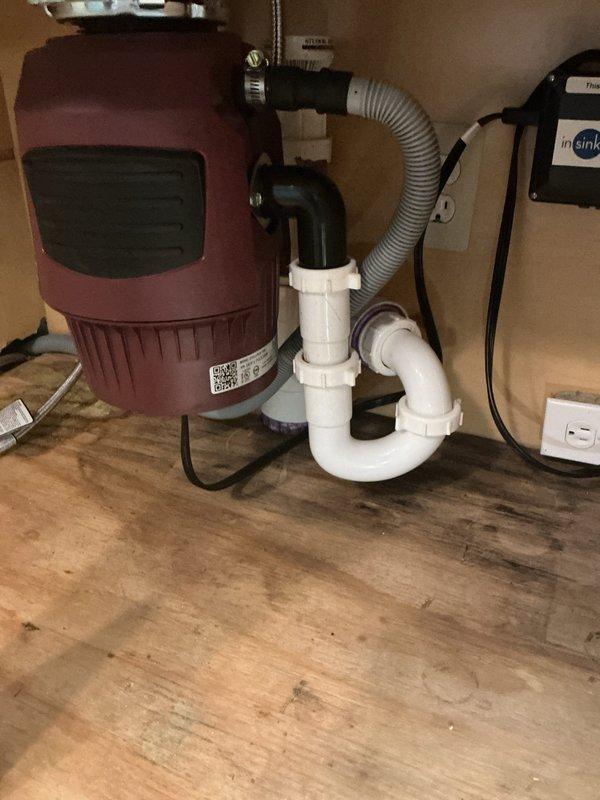 Responded to complete kitchen sink blockage in 1998-built residence where previous DIY attempts including garbage disposal replacement, P-trap disassembly, 10-15 ft cable snaking, and chemical treatments had failed to resolve the issue. Upon inspection, verified new InSinkErator disposal installation and existing white PVC drain configuration beneath single-bowl stainless steel sink. Performed advanced drain clearing procedures beyond the initial 15 feet of line previously attempted, successfully locating and removing obstruction in main drain line that had caused progressive drainage deterioration over the preceding week. Tested system flow through disposal unit and drain assembly, confirming full restoration of drainage capacity and proper operation of all components.