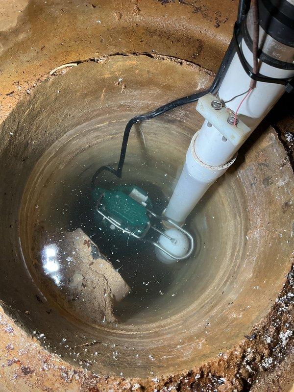 Completed sump pump replacement in basement of 45-year-old residential property. Removed existing submersible pump unit from circular basin showing significant age-related deterioration, mineral deposits, and water staining. Installed new submersible sump pump with float switch mechanism, secured vertical PVC discharge piping with proper couplings and support brackets, and verified electrical connections. System tested and operational; provided warranty information to homeowner as requested.