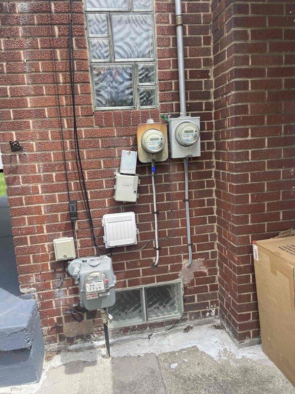 Conducted comprehensive site evaluation for complete air conditioning system replacement at residential property. Assessed existing outdoor AC unit of unknown age and documented current installation configuration. Inspected interior basement/garage area with concrete block walls where HVAC components interface with structure, noting exposed ceiling joists and available mounting points for new equipment. Evaluated exterior utility connections including electrical service panels, gas meter, and existing conduit routing on brick facade. Documented glass block window locations and clearance requirements for equipment access and ventilation. Photographed all relevant areas to determine proper equipment sizing, electrical service capacity, refrigerant line routing options, and condensate drainage requirements. Provided customer with detailed replacement system recommendations and installation specifications.