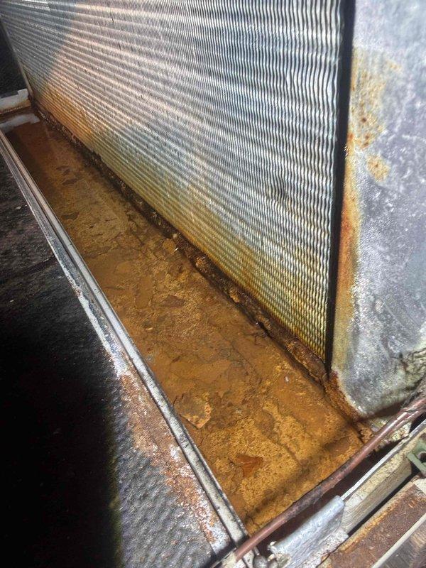 Completed Gold AC inspection on 23-year-old air conditioning system with air handler located in attic. Performed comprehensive evaluation of all system components, including examination of evaporator coil which showed significant accumulation of dirt and debris on mesh filter screen and collection pan with rust-colored sediment buildup. Inspected ductwork support structure and verified proper installation of HVAC components in attic space. System is currently operational but exhibits signs of age-related wear and requires attention to maintain efficiency and prevent potential failures.