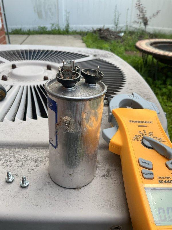 Responded to no cooling complaint on 7-year-old residential air conditioning system located at rear of property. Upon arrival, performed diagnostic testing on outdoor condenser unit using digital multimeter to assess electrical components. Testing revealed failed dual run capacitor showing signs of corrosion, discoloration, and terminal degradation. Capacitor tested outside acceptable microfarad range, preventing compressor and condenser fan motor from operating. Removed defective capacitor from electrical compartment, disconnected wiring from terminals, and installed new replacement capacitor with proper microfarad rating. Secured all electrical connections, verified proper wire routing, and reassembled unit housing. Cycled system through complete startup sequence, confirmed compressor engagement, verified condenser fan operation, and measured proper voltage and amperage at all components. System restored to normal cooling operation with all components functioning within manufacturer 