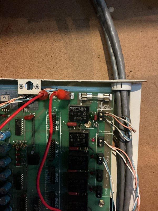 Responded to no cooling call on 3-year-old system with zone control. Previous technician had bypassed circuit board protection with jumper wire, and required fuse was never provided to homeowner. Inspected zone control board in basement and documented current wiring configuration showing multiple zone relays and damper controls. System inoperable due to improper previous repair and missing overcurrent protection device.