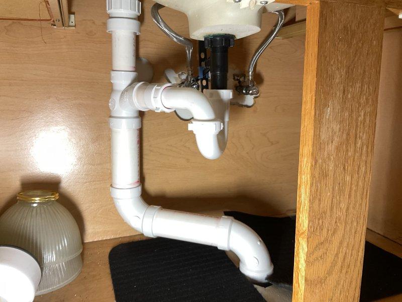 Completed plumbing inspection and testing of kitchen sink drainage system and bathroom lavatory faucet. Kitchen cabinet plumbing showed proper P-trap configuration with white PVC drainage assembly connected to garbage disposal unit, braided stainless steel supply lines in good condition, and dishwasher drain connection properly installed. Verified bathroom faucet functionality with water flow test confirming proper operation of chrome center-set fixture with dual handles and adequate drainage through basin assembly.