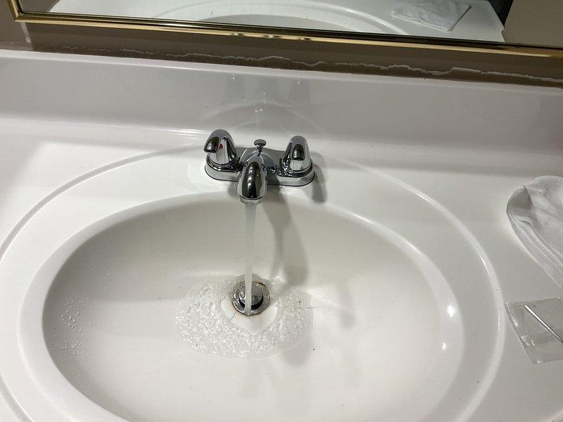 Completed plumbing inspection and testing of kitchen sink drainage system and bathroom lavatory faucet. Kitchen cabinet plumbing showed proper P-trap configuration with white PVC drainage assembly connected to garbage disposal unit, braided stainless steel supply lines in good condition, and dishwasher drain connection properly installed. Verified bathroom faucet functionality with water flow test confirming proper operation of chrome center-set fixture with dual handles and adequate drainage through basin assembly.