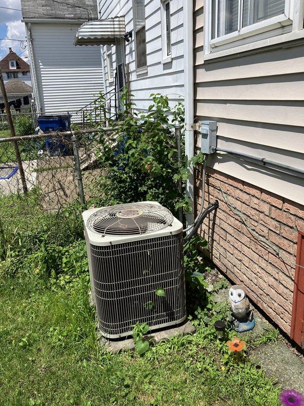 Conducted comprehensive site evaluation for complete HVAC system replacement including new central air conditioning unit and furnace installation. Assessed existing outdoor condenser unit positioned against residential exterior, noting vegetation growth around equipment and current electrical disconnect configuration. Evaluated interior and exterior conditions to determine ductwork requirements and identify potential modifications needed for new system installation. Documented existing equipment specifications and mounting locations through photographic documentation to support proposal development for full system upgrade.
