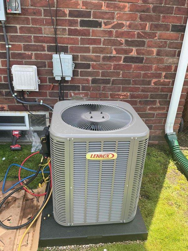 Completed installation of 2-ton Lennox air conditioning system with matching evaporator coil at rear of property. Unit was positioned on concrete pad against brick wall with proper electrical disconnect and conduit installation, refrigerant lines connected and charged, and condensate drainage line installed across lawn area. All mechanical, electrical, and air conditioning permits were obtained, system was tested for proper operation, and existing connections were successfully reconnected to complete the installation.