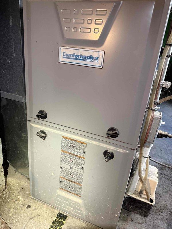 Responded to no cooling complaint on 10-year-old Comfortmaker furnace and air conditioning system located in basement. Upon arrival, confirmed customer reports of loud noises from equipment during operation. Performed diagnostic inspection of both furnace cabinet and AC components. Inspected control board wiring connections and found multiple wire terminals with dust accumulation and signs of age-related wear. Examined furnace cabinet panels, ventilation slots, and exterior components for operational integrity. Documented existing control board configuration showing cream-colored PCB with multiple colored wire connections including red, blue, white, pink, yellow, and green leads connected through terminal blocks. Photographed current system condition including control board placement near ductwork and copper refrigerant lines. Assessed overall equipment status and provided recommendations for addressing noise concerns and ensuring continued system operation.