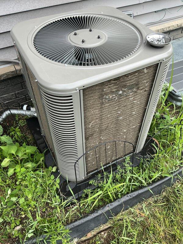 Completed comprehensive Gold AC inspection on residential single-zone air conditioning system less than one year old with air handler located in basement. Performed thorough visual assessment of outdoor condenser unit, documenting equipment condition through detailed photography. Inspection revealed significant accumulation of dirt, dust, and debris on exterior condenser coils and filter surfaces, as well as overgrown vegetation around unit base requiring attention for optimal airflow and system efficiency. Verified system operational status, examined fan assembly and mounting hardware, and assessed overall equipment condition. Unit currently functioning properly despite maintenance needs identified during inspection.