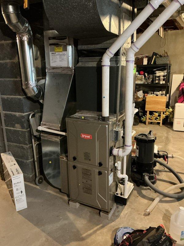 Completed comprehensive Gold AC inspection on 4-year-old Bryant HVAC system with air handler located in basement. Performed full system evaluation including thermostat operation verification (Sensi digital unit displaying 69°F), inspected furnace unit and associated components, checked PVC condensate drainage and venting systems, examined ductwork and plenum connections, and verified proper clearances around equipment. Inspected outdoor condenser unit and advised customer to maintain clear area around condenser free of debris and animal waste. All system components operational and accessible for maintenance. Documentation completed with photographic records of thermostat controls and basement mechanical equipment installation.