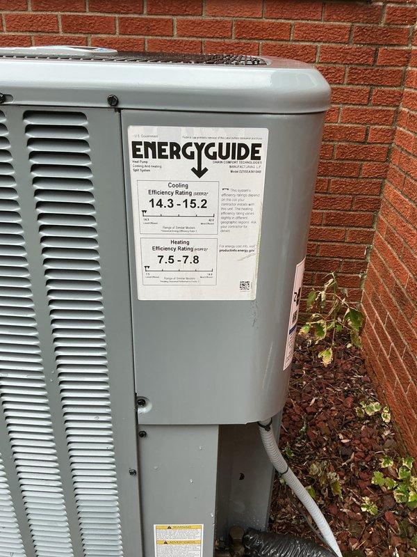 Completed comprehensive Gold AC Inspection on a 2-year-old residential heat pump system with SEER rating of 14.3-15.2 and HSPF rating of 7.5-7.8. Performed visual inspection of outdoor condensing unit positioned against brick foundation, verifying proper clearances and examining electrical disconnect box with associated conduit connections. Documented system specifications via EnergyGuide label and assessed overall equipment condition, noting unit mounted on mulch bed with adequate drainage via PVC condensate line.