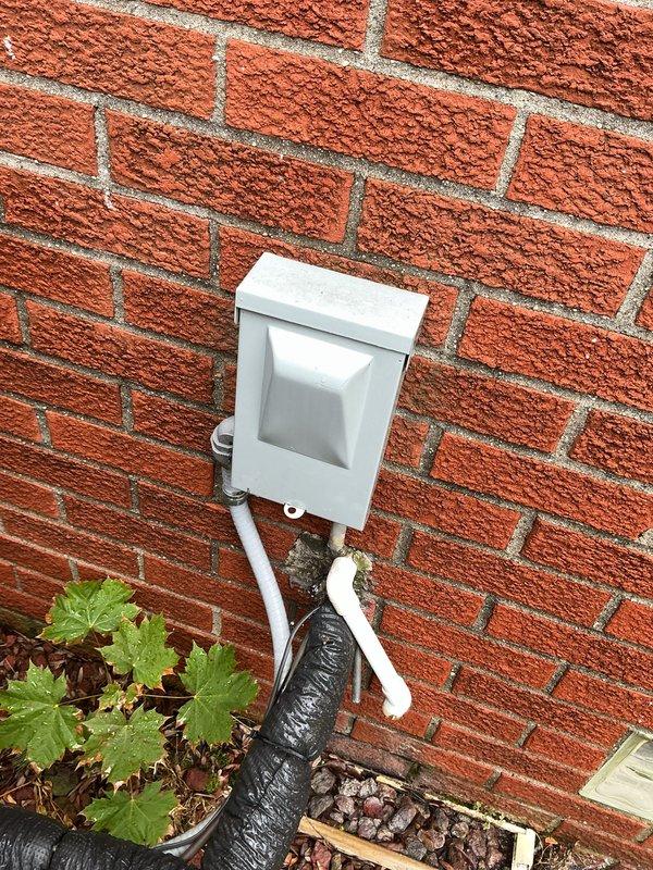 Completed comprehensive Gold AC Inspection on a 2-year-old residential heat pump system with SEER rating of 14.3-15.2 and HSPF rating of 7.5-7.8. Performed visual inspection of outdoor condensing unit positioned against brick foundation, verifying proper clearances and examining electrical disconnect box with associated conduit connections. Documented system specifications via EnergyGuide label and assessed overall equipment condition, noting unit mounted on mulch bed with adequate drainage via PVC condensate line.