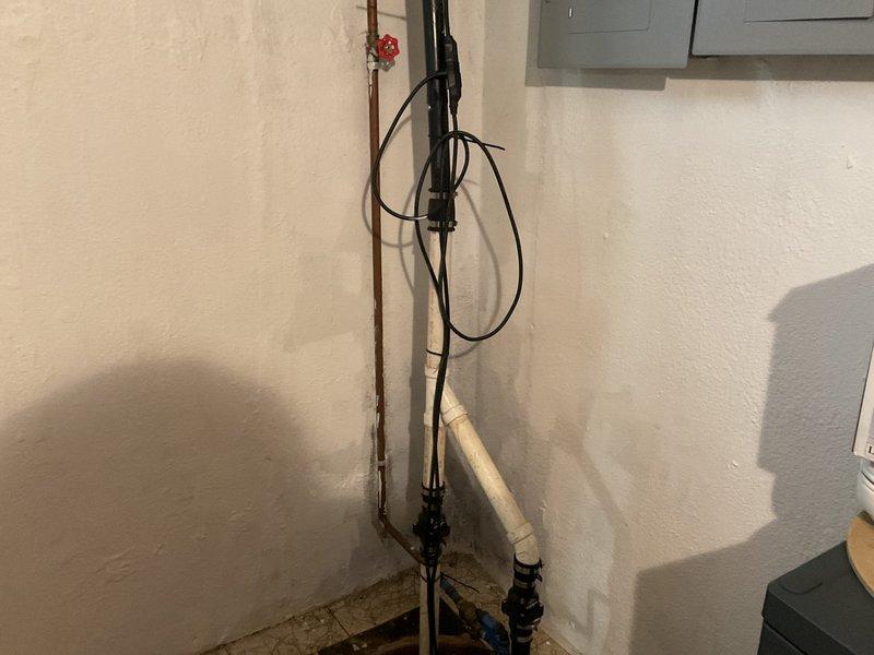 Provided estimate for sump pump upgrade in basement of 53-year-old home. Assessed existing sump pump system with failed water-powered backup that experienced mineral deposit buildup. Evaluated current installation including primary pump, discharge piping with PVC and copper components, check valves, and electrical connections. Discussed battery backup system options to replace water backup due to previous failure and concerns about power outages from recent storms. Photographed existing setup showing vertical discharge piping with shut-off valve, electrical conduit, sump pit with active water level, and tile floor installation around pit opening. Presented upgrade recommendations for battery-operated backup sump pump system to provide reliable secondary pumping capacity during power failures without dependency on municipal water pressure.