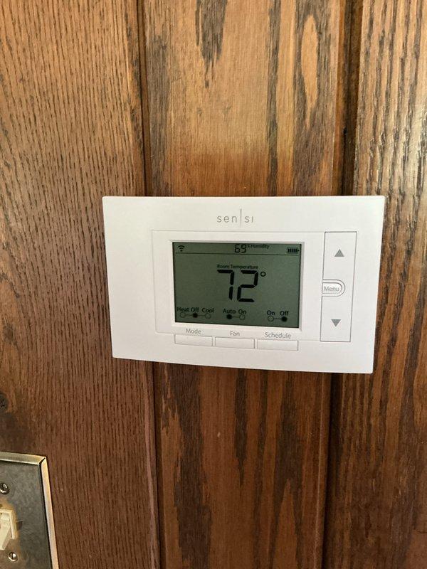 Completed comprehensive Gold AC inspection on 2025 single-unit system with air handler located in basement. Verified system operational status at thermostat showing 72° and confirmed proper temperature control functionality. Inspected outdoor condenser unit positioned on rubber pad against exterior wall, noting adequate clearance and ventilation through louvers and top-mounted fan assembly, with minor debris accumulation around base requiring attention for optimal airflow and performance.