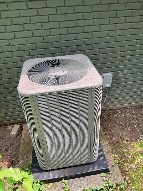 Completed comprehensive Gold AC inspection on 2025 single-unit system with air handler located in basement. Verified system operational status at thermostat showing 72° and confirmed proper temperature control functionality. Inspected outdoor condenser unit positioned on rubber pad against exterior wall, noting adequate clearance and ventilation through louvers and top-mounted fan assembly, with minor debris accumulation around base requiring attention for optimal airflow and performance.
