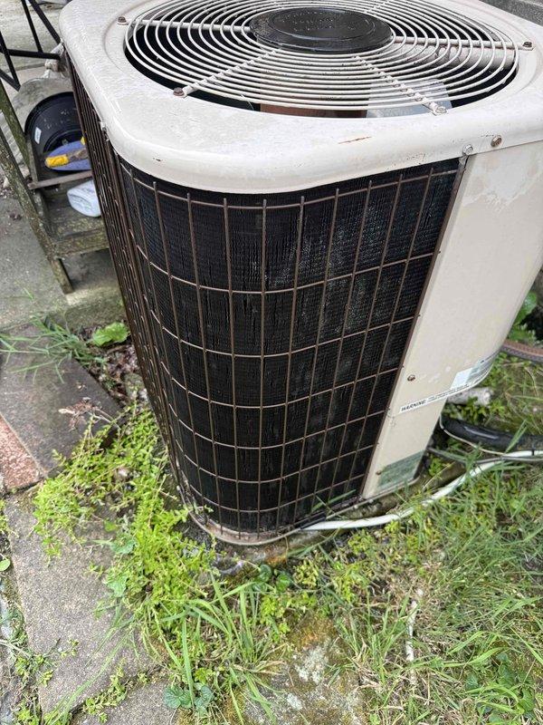 Completed comprehensive Gold AC inspection on 26-year-old outdoor condensing unit. Performed electrical diagnostics using clamp meter to verify amperage draw and system performance. Inspected condenser coils through mesh grille, noting unit's age and weathered exterior condition. Evaluated fan assembly operation and overall system functionality. Unit currently operational with air handler/coil located in basement. Documented equipment condition with photographic evidence showing outdoor condenser positioned on concrete pad with surrounding vegetation growth and minor debris accumulation at base.