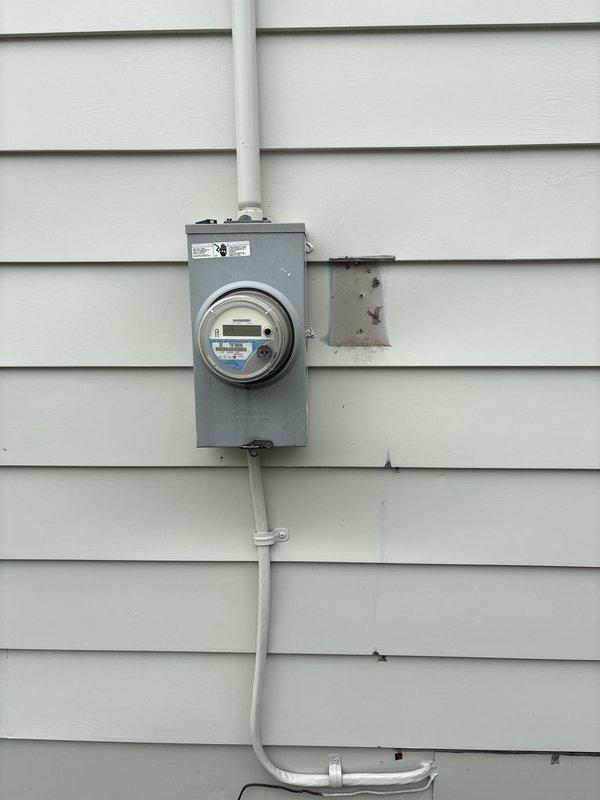 Completed full HVAC system installation including a 70,000 BTU furnace and 2-ton air conditioning unit positioned in the left side yard. Installation included humidifier integration, electrical and mechanical permits, reconnection of existing utilities, and proper condensate drainage with PVC trap assembly. System tested and operational with digital meter readings confirming proper voltage and amperage, AHRI certification number 215663144 documented, and customer qualified for utility rebate programs through Consumers Energy and DTE.