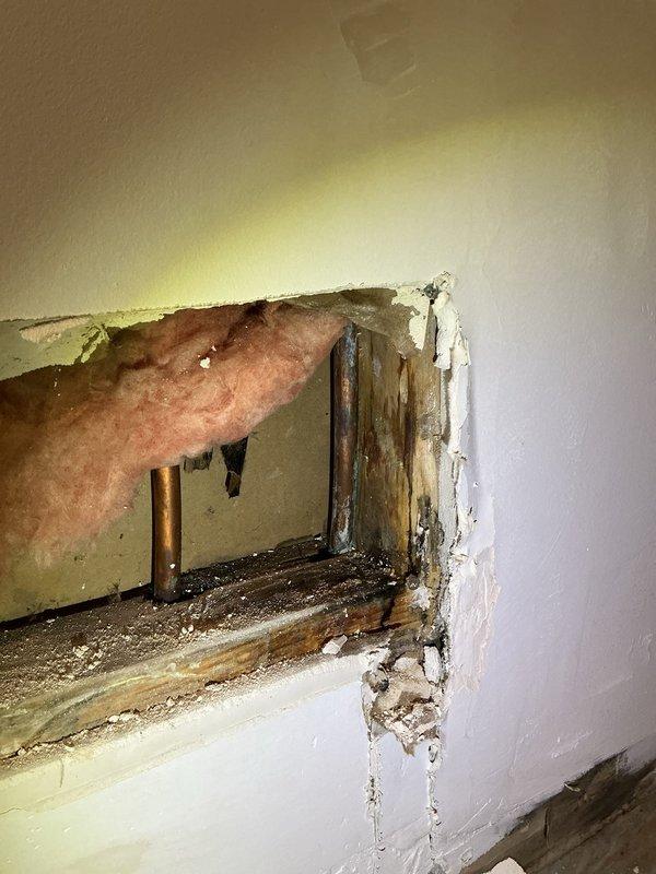 Responded to water leak originating from humidifier installation located in attic over garage. Upon inspection, discovered active leak had caused significant water damage to interior wall and structural framing. Documented extensive water staining, compromised drywall, and moisture damage to wooden structural members with visible discoloration and deterioration. Exploratory opening revealed darkened framing and saturated building materials at base of affected wall. Traced leak source to one-year-old humidifier unit and identified improper installation as root cause of water intrusion. Shut down humidifier system to prevent further damage and recommended immediate remediation of affected areas and reinstallation per manufacturer specifications.