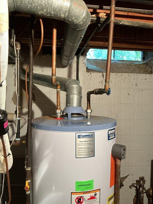 Responded to reported water leak suspected to originate from water heater in basement utility area. Upon inspection, examined Kenmore water heater unit and surrounding plumbing connections, including copper supply lines, pressure relief valve, and associated pipe fittings at top of tank. Assessed all visible connections, valves, and tank exterior for signs of active leakage or moisture accumulation. Documented existing plumbing configuration including PVC drainage lines, galvanized ductwork, and expansion tank installation. Verified proper operation of water heater components and identified source of reported leak condition.