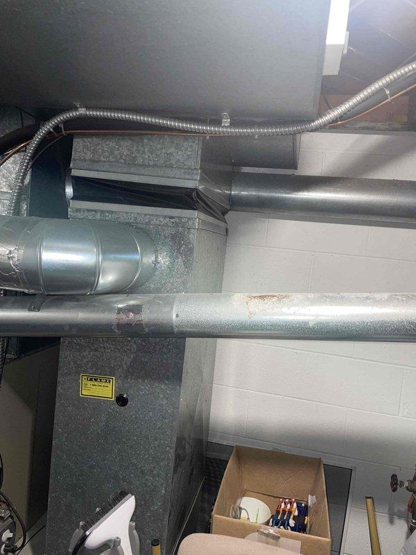 Completed full system estimate on 27-year-old Lennox HVAC system following annual AC tune-up and cooling maintenance inspection. System confirmed operational upon arrival. Evaluated complete installation including gray metal air handler unit, metallic ductwork with flexible corrugated sections, and beige Teton Air Bear filtration component located in basement utility area. Assessed condition of existing equipment showing age-related wear including minor surface oxidation on horizontal ductwork and visible rust spots on metallic surfaces. Documented current system configuration with white concrete block walls and concrete flooring typical of mechanical room installations. Provided comprehensive estimate options for full system replacement considering equipment age and observed wear patterns on existing components.