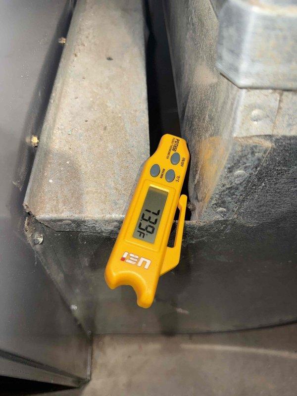 Performed comprehensive inspection and tune-up on 27-year-old residential air conditioning system located in backyard. Evaluated condenser unit which exhibited significant rust corrosion on exterior cabinet panels and fastener points, indicating advanced age and weathering. Measured supply air temperature at 96.9°F using calibrated digital thermometer at ductwork. Inspected condenser coils through front grille mesh, assessed refrigerant lines and electrical conduit connections. Examined thermostat operation and verified proper communication with cooling system. Conducted visual inspection of humidifier components and hot water tank as part of complete home comfort system evaluation. Unit showed signs of considerable deterioration consistent with its age, including rust staining, paint degradation, and general wear on cabinet surfaces. Provided assessment of remaining equipment lifespan based on observed condition of condenser unit, internal components, and overall system performance. A