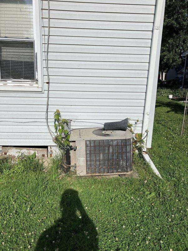 Completed estimate for replacement of aging outdoor air conditioning condenser unit currently utilizing obsolete R22 refrigerant. The existing beige metal-grilled unit showed visible weathering and age-related deterioration, positioned on grass against vinyl siding with standard electrical conduit installation. Assessment included evaluation of indoor climate control system featuring Honeywell Home digital thermostat and Aprilaire humidistat for compatibility with replacement equipment recommendations.