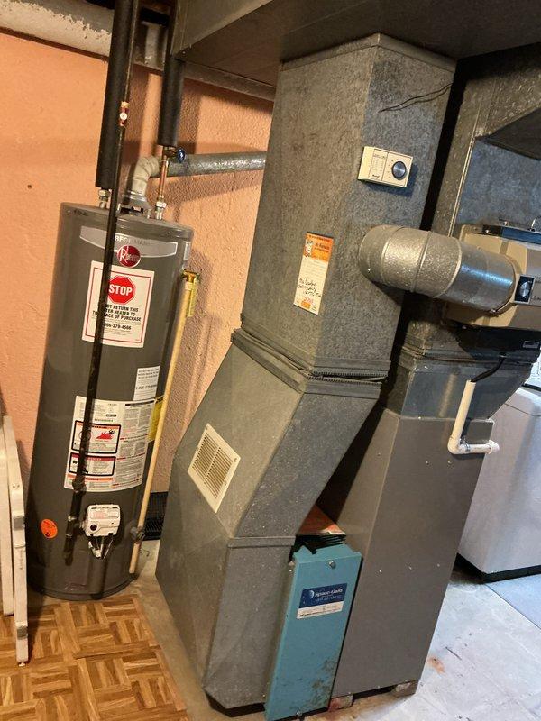 Responded to service call for central air conditioning system not cooling. Upon inspection, discovered cracked heat exchanger in furnace unit located in basement utility area. Evaluated complete HVAC system including 10-year-old outdoor AC unit installed in 2018. Documented equipment condition through photography showing furnace with cylindrical blower housing, Aqua-Gard water treatment component, and associated ductwork. Provided comprehensive estimate for full system replacement due to failed heat exchanger and aging air conditioning equipment.