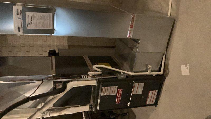 Responded to complaint of loud noise from furnace/AC system during startup and shutdown, along with delayed AC operation. Inspected 9-year-old air conditioning system located in basement and found noise consistent with thermal expansion and contraction of ductwork, which is normal during temperature changes in the system. Verified AC unit operational with adequate cooling capacity, checked refrigerant lines and connections for proper installation and support, and confirmed all mechanical components functioning within normal parameters. Documented system condition with photographs showing air handler, ductwork, and associated plumbing infrastructure.