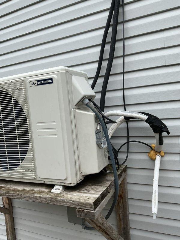 Performed service call on 3-year-old Blueridge mini split system located in garage/ADU. Upon arrival, conducted thorough inspection of outdoor condensing unit and refrigerant line set installation. System was operational with cooling capacity intact and no reported loss of function. Visually inspected condenser unit mounted on exterior wooden platform, verifying secure mounting and proper clearances. Examined refrigerant line set routing along building exterior, checking insulation integrity and mounting bracket security. Inspected condensate drain line installation including PVC routing and termination point. Verified electrical conduit connections and proper strain relief at unit. No immediate mechanical or refrigerant issues identified during inspection. System operating within normal parameters at time of service.