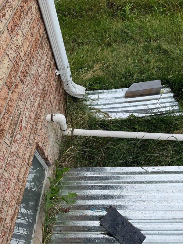 Conducted comprehensive drainage evaluation for property experiencing chronic water saturation and standing water issues in backyard area. Assessed existing sump pump discharge system and surrounding drainage infrastructure, including downspout configurations and ground-level water management components. Documented current conditions with photographic evidence showing wet pavement surfaces, saturated mulch beds, and existing PVC discharge piping along building foundation. Identified contributing factors to prolonged water retention and evaluated impact of previously redirected water from adjacent property. Provided recommendations for permanent drainage solution to address ongoing saturation problems and improve water diversion away from structure.