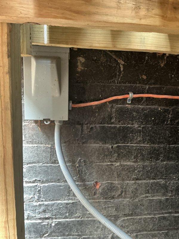 Responded to no cooling complaint on 2012 air conditioning system with outdoor condenser unit located beneath deck structure. Upon inspection, found unit blowing warm air and performed diagnostic evaluation of electrical connections, refrigerant levels, and compressor operation. Documented equipment condition and installation location in basement area with photos showing condenser placement and associated electrical components including junction box and conduit routing.