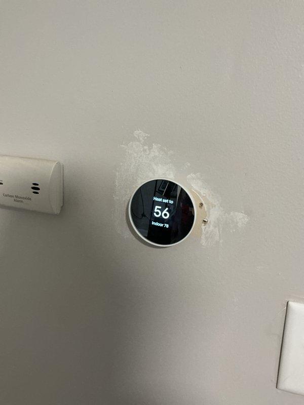 Conducted site assessment for new central air conditioning system installation at property with no existing AC equipment. Evaluated interior thermostat location and documented current heating system controls, noting existing smart thermostat set at 56°F heat setpoint with indoor temperature reading 73°F. Inspected basement utility area with painted concrete block walls to determine optimal routing for refrigerant lines, condensate drainage, and electrical connections. Discussed outdoor condenser unit placement options with property owner to determine most suitable location for equipment installation. Documented wall conditions near existing HVAC controls and assessed structural considerations for new system integration with current heating infrastructure.