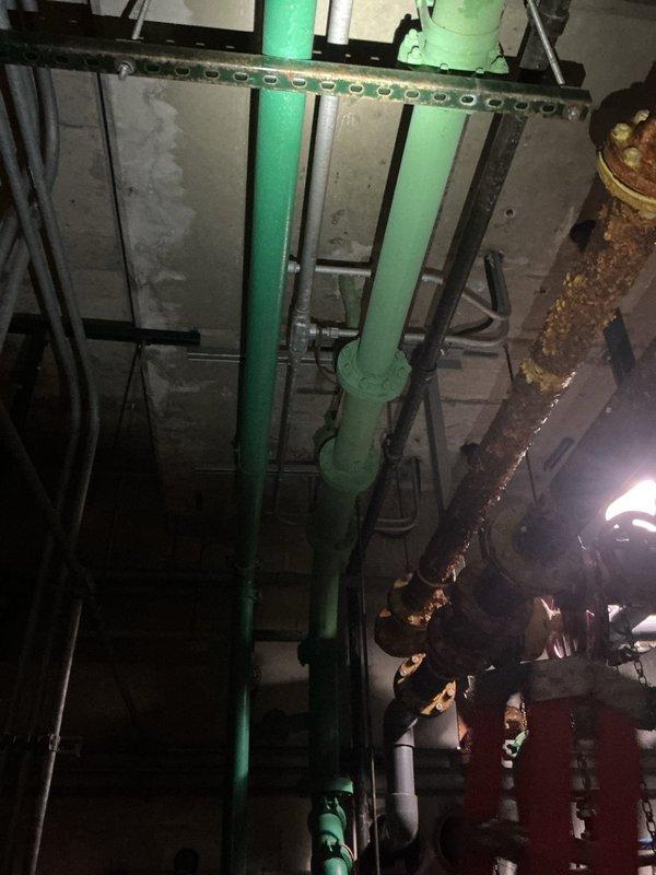 Performed commercial backflow prevention device testing on single unit as requested. Upon arrival, accessed mechanical room and located backflow assembly within overhead piping system featuring yellow and green painted pipes with multiple valve configurations and brass fittings. Conducted standard testing procedures on the backflow preventer, verified proper operation of check valves and relief valve, and documented system condition with photographic evidence showing the installation environment and equipment location within the facility's plumbing infrastructure.