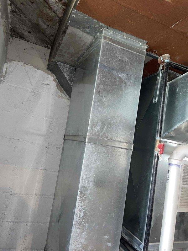 Conducted on-site assessment for central air conditioning system replacement. Evaluated existing HVAC infrastructure including main supply plenum, ductwork configuration, and current thermostat control system. Documented equipment location in mechanical room showing aged galvanized metal ductwork with dust accumulation and existing ceiling penetrations. Photographed thermostat mounting location and surrounding wall conditions to determine compatibility requirements for new system installation. Provided comprehensive estimate for complete central air conditioning system replacement based on existing duct infrastructure and space requirements.