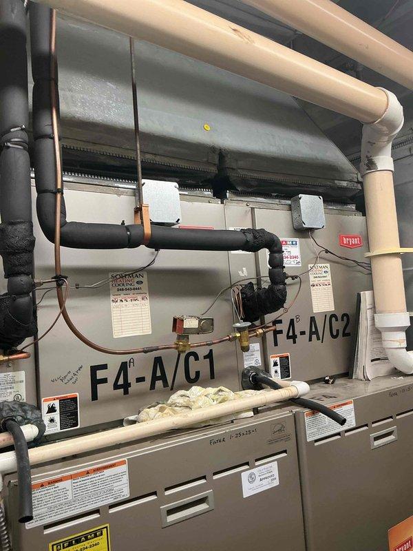 Completed full system replacement of two commercial Bryant RTUs (F4-A/C1 and F4-A/C2) in first-floor vacant lease space mechanical room with direct alley access. Reclaimed and properly recycled refrigerant from existing F1 and F4 condensers and cased coils. Coordinated 40-ton boom crane lift from alley for equipment removal and installation of like-for-like Bryant replacement units. Flushed and pressure tested all refrigerant line sets to verify system integrity. Updated liquid line insulation to meet current specifications. Completed all mechanical and electrical reconnections for both rooftop units, including refrigerant lines, condensate drainage systems, and power supplies. Verified proper operation of all components, controls, and safety devices. Both units labeled and operational with full piping infrastructure including black insulated suction lines, copper refrigerant piping, and white PVC condensate drains properly installed and secured.