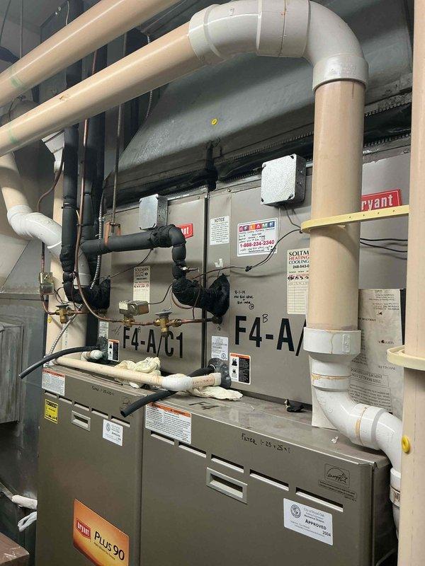 Completed full system replacement of two commercial Bryant RTUs (F4-A/C1 and F4-A/C2) in first-floor vacant lease space mechanical room with direct alley access. Reclaimed and properly recycled refrigerant from existing F1 and F4 condensers and cased coils. Coordinated 40-ton boom crane lift from alley for equipment removal and installation of like-for-like Bryant replacement units. Flushed and pressure tested all refrigerant line sets to verify system integrity. Updated liquid line insulation to meet current specifications. Completed all mechanical and electrical reconnections for both rooftop units, including refrigerant lines, condensate drainage systems, and power supplies. Verified proper operation of all components, controls, and safety devices. Both units labeled and operational with full piping infrastructure including black insulated suction lines, copper refrigerant piping, and white PVC condensate drains properly installed and secured.