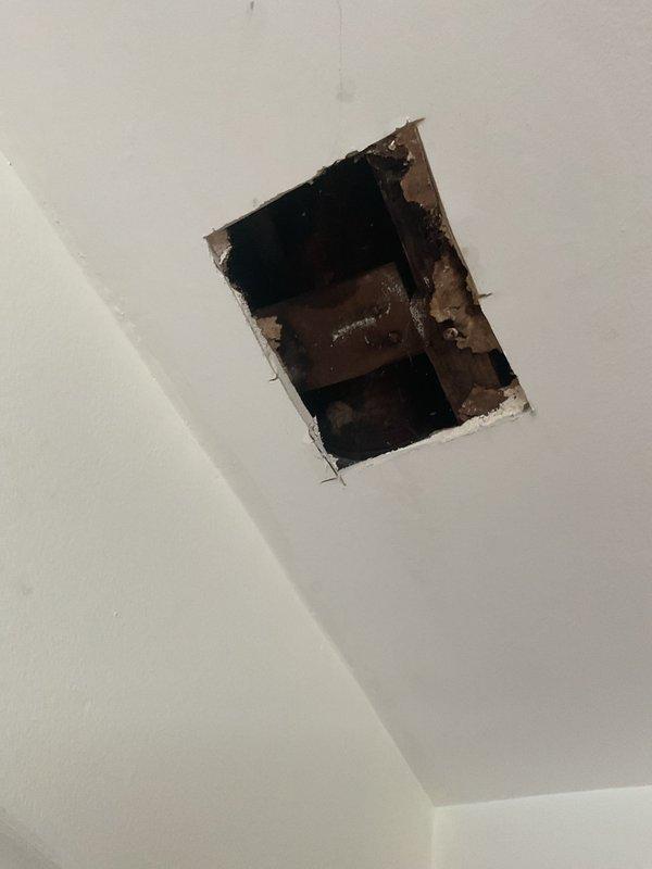 Responded to second-floor toilet leak causing water damage to ceiling below. Upon arrival, inspected affected bathroom with white porcelain two-piece toilet and assessed ceiling damage in room directly underneath. Found active leak originating from toilet fixture requiring access through first-floor ceiling for proper diagnosis and repair. Cut rectangular access opening in ceiling drywall to expose wooden joists and plumbing connections above. Identified source of water intrusion at toilet base or supply line connection. Repaired faulty seal/connection to stop active leak. Verified repair by testing toilet operation and checking for additional moisture. Access opening left for customer to arrange drywall repair and finishing. Leak successfully stopped, preventing further water damage to ceiling and structure.