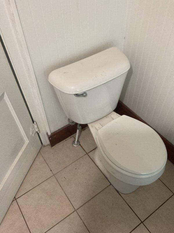 Responded to second-floor toilet leak causing water damage to ceiling below. Upon arrival, inspected affected bathroom with white porcelain two-piece toilet and assessed ceiling damage in room directly underneath. Found active leak originating from toilet fixture requiring access through first-floor ceiling for proper diagnosis and repair. Cut rectangular access opening in ceiling drywall to expose wooden joists and plumbing connections above. Identified source of water intrusion at toilet base or supply line connection. Repaired faulty seal/connection to stop active leak. Verified repair by testing toilet operation and checking for additional moisture. Access opening left for customer to arrange drywall repair and finishing. Leak successfully stopped, preventing further water damage to ceiling and structure.