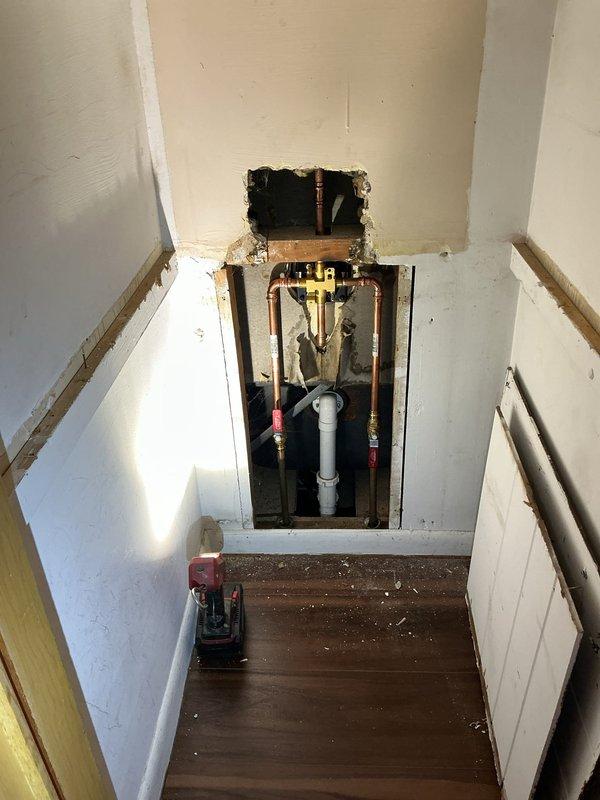 Responded to a broken faucet located behind the wall near the ceiling in a 50-year-old residence. Performed wall access by cutting drywall to expose the concealed plumbing system, revealing copper hot and cold water supply lines with shut-off valves and PVC drainage piping. Repaired the compromised faucet assembly, verified proper water flow and pressure at the tub-shower fixtures, and confirmed all connections were secure with no active leaks.