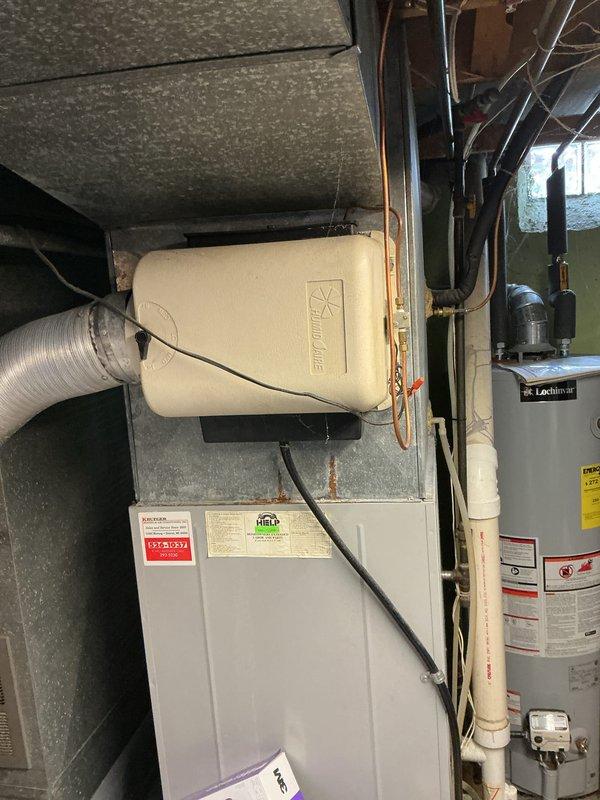 Completed estimate for replacement of 30-year-old furnace and air conditioning system. Furnace unit located in basement mechanical room with existing humidifier attachment, air conditioner positioned in backyard. Both units have reached end of expected service life and customer requested replacement pricing. Photographed existing equipment including furnace with mounted humidifier, electrical panel, and overall installation configuration for accurate system sizing and replacement planning.