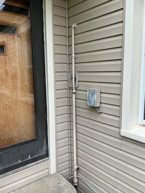 Completed gas line repair work at residential property with active construction in area. Inspected and serviced vertical gas piping system running along exterior corner of home, addressing rust staining and corrosion at lower connection point near valve assembly. Evaluated basement gas line configuration including aged galvanized piping with T-junction connections showing surface oxidation and dust accumulation. Verified proper mounting and support brackets on exterior PVC vent piping. Assessed structural clearances around gas lines passing through floor joists in crawl space area. All work performed in accordance with applicable gas fitting codes and safety standards.