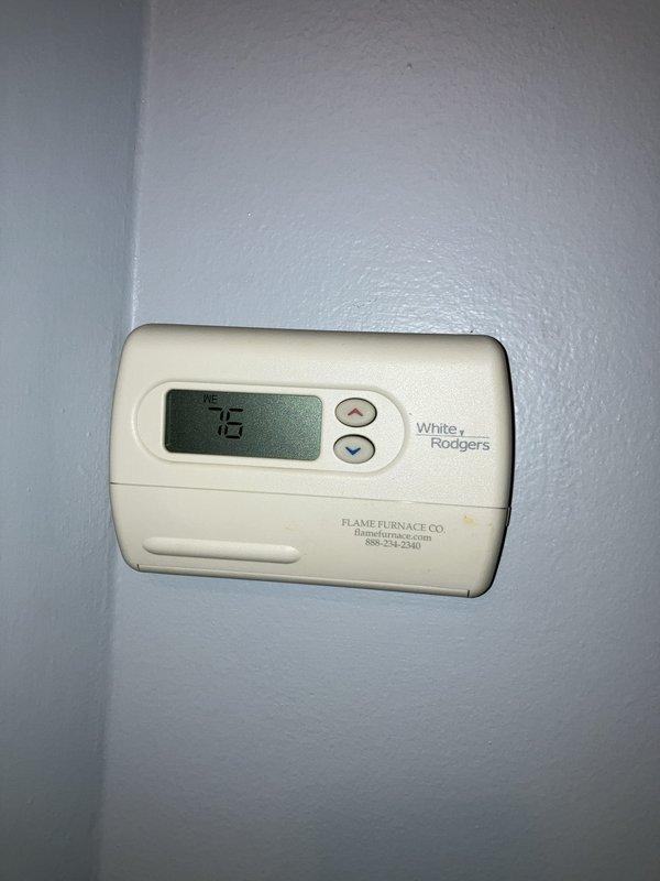 Completed full system estimate for approximately 20-year-old air conditioning system located on side of property. Inspected outdoor condenser unit with cylindrical design and top-mounted fan assembly, noting beige exterior housing with vertical slat venting, mounted on concrete pad with proper clearance from brick wall and electrical disconnect box. Evaluated White-Rodgers thermostat with digital display showing current temperature setting. Assessed overall system condition and provided comprehensive replacement estimate due to advanced age of equipment, as routine maintenance was originally requested but full system evaluation determined replacement recommendations necessary for aging HVAC infrastructure.