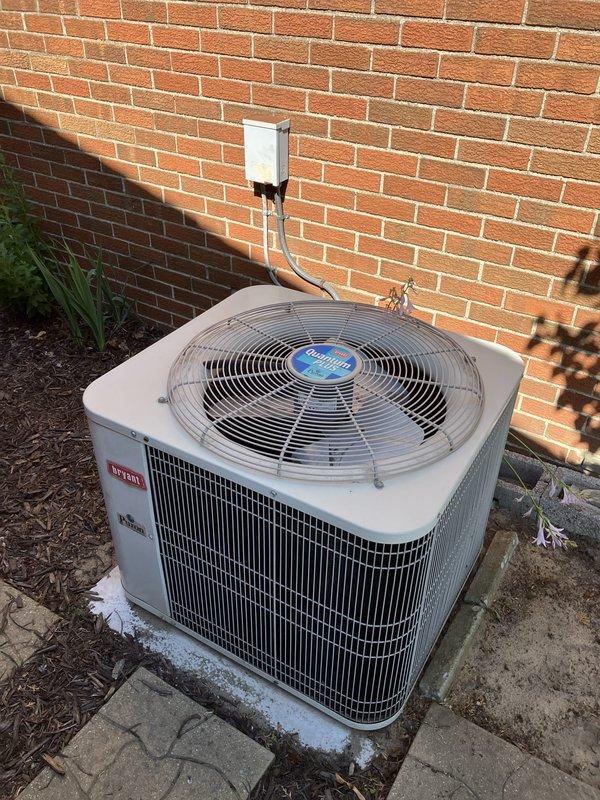 Completed full system estimate for approximately 20-year-old air conditioning system located on side of property. Inspected outdoor condenser unit with cylindrical design and top-mounted fan assembly, noting beige exterior housing with vertical slat venting, mounted on concrete pad with proper clearance from brick wall and electrical disconnect box. Evaluated White-Rodgers thermostat with digital display showing current temperature setting. Assessed overall system condition and provided comprehensive replacement estimate due to advanced age of equipment, as routine maintenance was originally requested but full system evaluation determined replacement recommendations necessary for aging HVAC infrastructure.