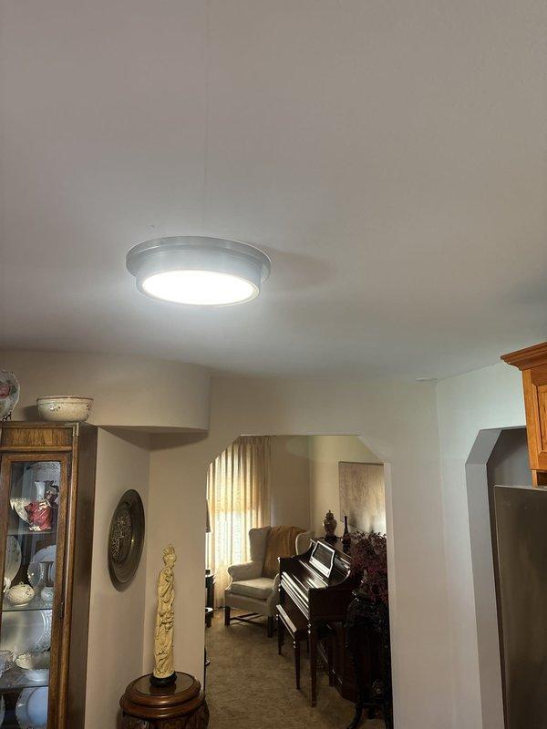 Installed two modern circular LED ceiling light fixtures in residential interior spaces. First fixture was mounted in main living area ceiling above music room, and second fixture was installed in hallway ceiling between bedroom access points. Both fixtures feature chrome-rimmed design with integrated LED panels, properly wired to existing electrical circuits, tested for functionality, and confirmed operational upon completion.