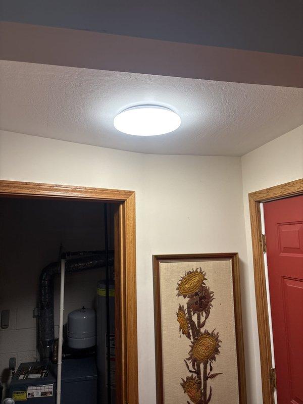 Installed two modern circular LED ceiling light fixtures in residential interior spaces. First fixture was mounted in main living area ceiling above music room, and second fixture was installed in hallway ceiling between bedroom access points. Both fixtures feature chrome-rimmed design with integrated LED panels, properly wired to existing electrical circuits, tested for functionality, and confirmed operational upon completion.