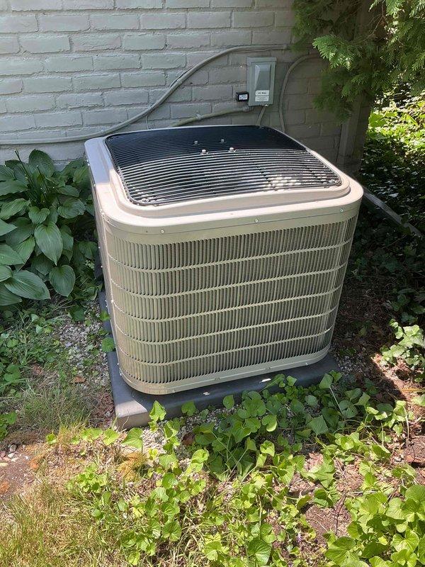 Completed comprehensive Gold AC inspection on a 6-year-old residential air conditioning system. Performed thorough examination of outdoor condenser unit positioned against exterior brick wall, verifying proper clearance from surrounding vegetation and adequate airflow around cabinet. Inspected electrical connections, disconnect box, and conduit routing for code compliance and secure mounting. Evaluated refrigerant line insulation and copper piping condition running along wall to basement air handler location. Checked condenser pad levelness and stability, confirmed fan grille integrity and protective components in place. Verified unit operational status with homeowner present, documenting equipment condition through photographic records. System found operating normally with clean exterior surfaces and intact housing, suitable for continued seasonal use.