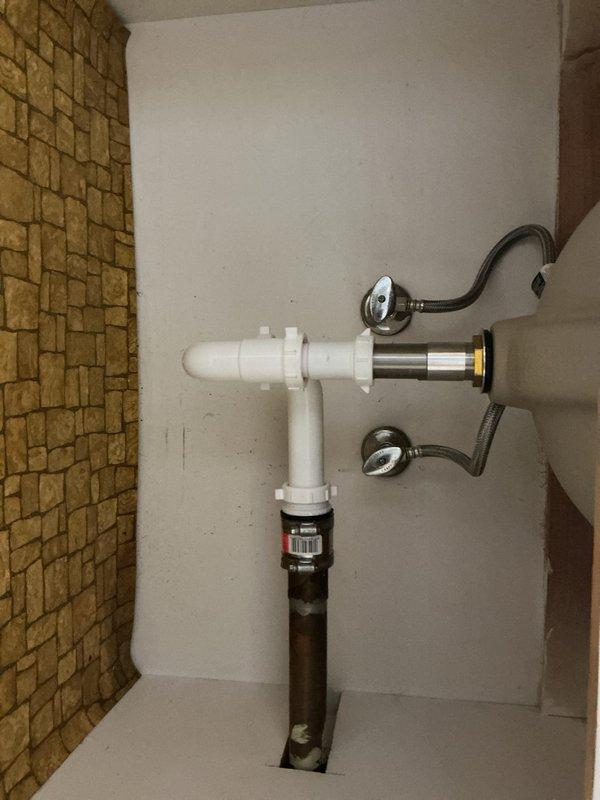 Installed new water heater with complete plumbing connections, including white PVC piping assembly configured in T-shape arrangement with pressure relief valve and flexible supply lines. Connected black discharge pipe extending to floor drain and verified all connections for proper operation and code compliance.