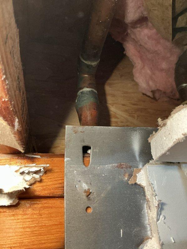 # Plumbing Access and Repair Work

Performed emergency plumbing access work requiring removal of interior drywall to reach concealed copper water supply lines. Cut and removed section of wall material to expose framing cavity containing aged copper piping showing significant oxidation and verdigris corrosion. Accessed plumbing system through wall cavity between vertical studs where insulation was present.

Inspected copper supply lines exhibiting advanced patina, rust-stained metal mounting brackets, and corrosion indicators requiring intervention. Work area was properly protected with drop cloths to contain debris during wall demolition and plumbing access procedures. Successfully exposed the compromised plumbing components for necessary repair or replacement, ensuring full access to the affected water supply infrastructure.