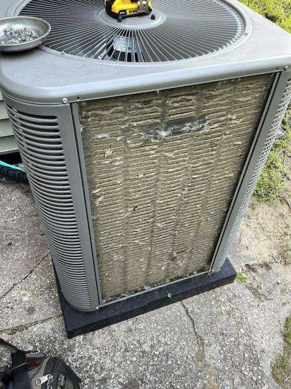 Completed comprehensive Gold AC inspection on 3-year-old residential air conditioning system with air handler located in basement. Performed thorough examination of outdoor condensing unit, which showed significant dirt and debris accumulation on coil surfaces and filter elements requiring attention. Inspected condenser cabinet, fan assembly with radial grille, and verified unit positioning on concrete pad with proper clearances. Evaluated electrical disconnect and conduit connections mounted on exterior wall. Assessed overall system operation and confirmed equipment was functioning at time of inspection. Documented heavy buildup of dust, dirt, and lint on front coil surfaces that could impact system efficiency and airflow if not addressed. Examined condenser coil fins through louvers and noted weathering consistent with outdoor installation. Verified fan guard integrity and checked for proper drainage around unit base. Inspected surrounding area for vegetation encroachment and debris 