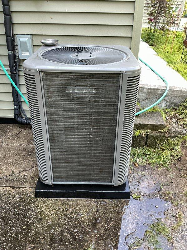 Completed comprehensive Gold AC inspection on 3-year-old residential air conditioning system with air handler located in basement. Performed thorough examination of outdoor condensing unit, which showed significant dirt and debris accumulation on coil surfaces and filter elements requiring attention. Inspected condenser cabinet, fan assembly with radial grille, and verified unit positioning on concrete pad with proper clearances. Evaluated electrical disconnect and conduit connections mounted on exterior wall. Assessed overall system operation and confirmed equipment was functioning at time of inspection. Documented heavy buildup of dust, dirt, and lint on front coil surfaces that could impact system efficiency and airflow if not addressed. Examined condenser coil fins through louvers and noted weathering consistent with outdoor installation. Verified fan guard integrity and checked for proper drainage around unit base. Inspected surrounding area for vegetation encroachment and debris 